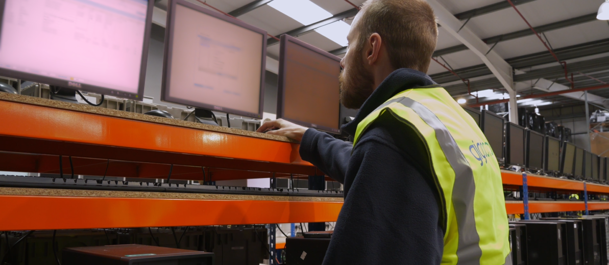 Technician in a neon safety vest checks computer monitors on an orange shelving rack in a data center.